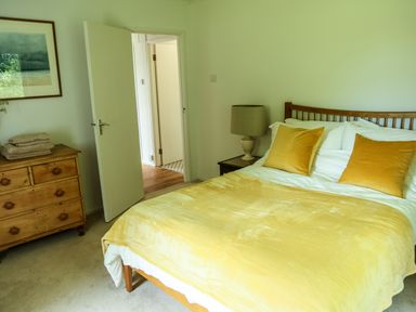 A bedroom with a bed with yellow pillows and blanket a bedside table with a lamp and a wooden chest of drawers at Henllys Lodge in Newport Pembrokeshire