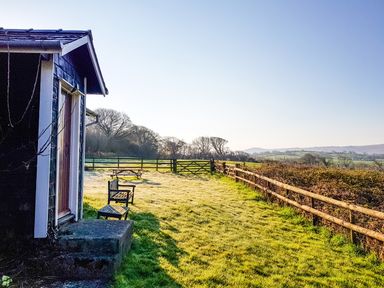 A backyard with a wooden bench and table next to a fenced grassy field at Henllys Lodge in Newport Pembrokeshire