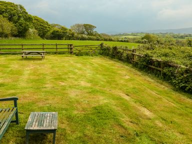 A fenced grassy yard with a wooden picnic table and bench overlooking fields and trees at Henllys Lodge Newport Pembrokeshire