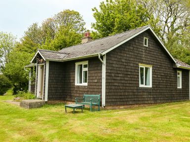 A brown wooden exterior house with white window frames and a green bench on the grass at Henllys Lodge in Newport Pembrokeshire