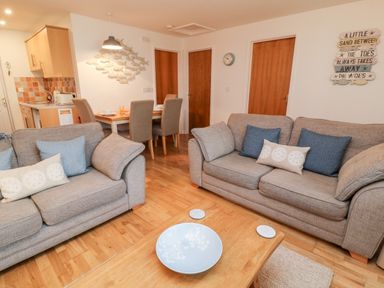 A living room with two sofas with cushions a wooden coffee table a dining table with chairs and kitchen area at Lilyvale in Davidstow near Camelford
