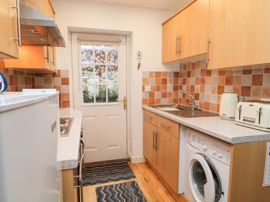 A kitchen with wooden cabinets a washing machine a toaster and kettle near a door at Lilyvale in Davidstow near Camelford