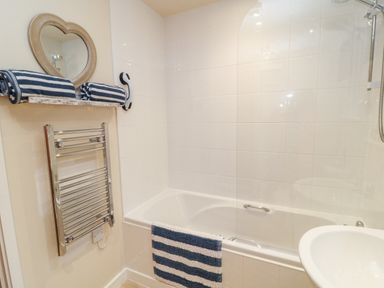 A bathroom with a bathtub sink striped towels towel rack and a heart shaped mirror at Lilyvale in Davidstow near Camelford