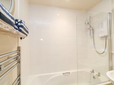 A bathroom with a bathtub a shower attached to the wall towels on a wooden shelf and a towel radiator at Lilyvale Davidstow near Camelford