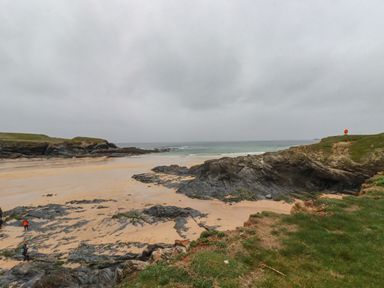 A rocky beach with sandy areas and grassy cliffs under a cloudy sky