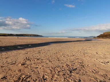 A sandy beach with a small stream flowing towards the sea with cliffs in the background at Lilyvale in Davidstow near Camelford