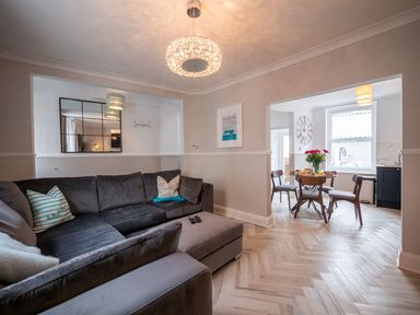 A living room with a gray sectional sofa and pillows opening to a dining area with a round table and chairs at Green Retreat in Dartmouth
