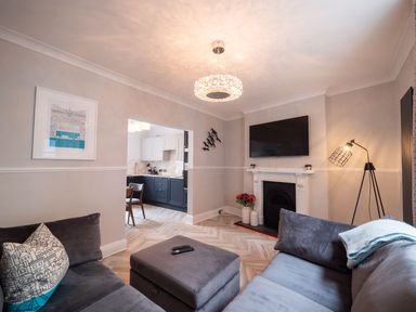 A living room with grey sofas a wall-mounted TV and a view into the kitchen at Green Retreat in Dartmouth