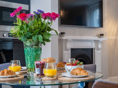 A dining table with orange juice croissants jam and flowers in a kitchen at Green Retreat in Dartmouth