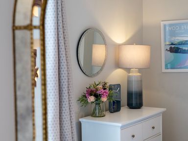 A white dresser with a lamp a clock a vase of flowers and a round mirror on the wall at Green Retreat in Dartmouth