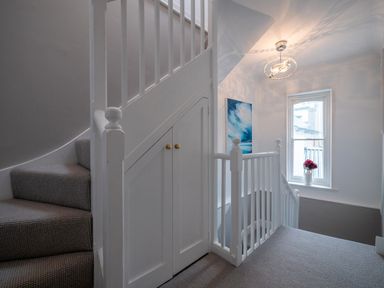 A staircase landing with carpeted stairs a white banister a storage cupboard under the stairs a window with flowers on the sill and a painting on the wall at Green Retreat in Dartmouth