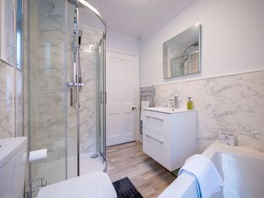 A bathroom with a curved glass shower, white vanity with sink, wall mirror, and bathtub at Green Retreat in Dartmouth