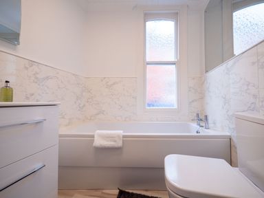 A bathroom with a bathtub under a frosted window a white vanity with a bottle on top and a toilet at Green Retreat in Dartmouth