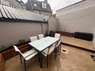 An outdoor patio with a glass table and six chairs next to brick planters and a storage box at Green Retreat in Dartmouth
