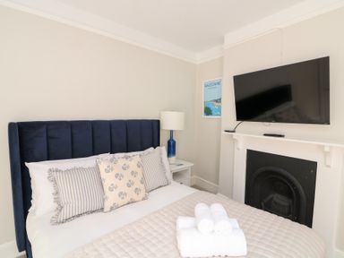 A bedroom with a blue headboard bed with pillows bedside table with lamp flat screen tv above a fireplace at Green Retreat in Dartmouth