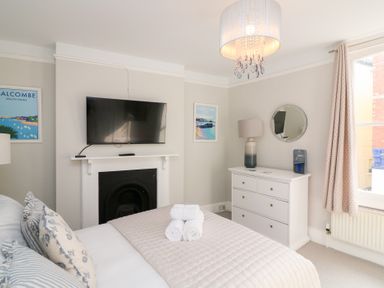 A bedroom with a bed with rolled towels a wall mounted tv a white chest of drawers and a window with curtains at Green Retreat in Dartmouth