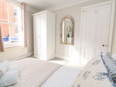 A bedroom with a white wardrobe a bed with pillows and folded towels a wall mirror and a window with curtains at Green Retreat in Dartmouth