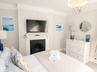 A bedroom with a bed, a television mounted above a fireplace, a dresser with a lamp and mirror, and two framed pictures at Green Retreat in Dartmouth