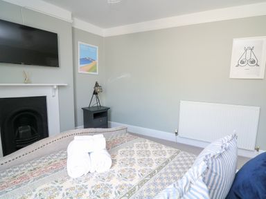 A bedroom with a bed with rolled towels on a patterned bedspread a black fireplace a wall-mounted TV a bedside table with a lamp and framed artwork on the walls at Green Retreat in Dartmouth