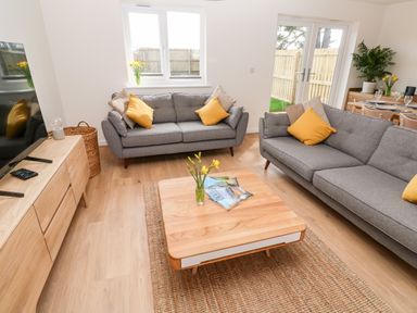 A living room with two gray sofas and a wooden coffee table with yellow flowers at The Bright House in St Eval near St Columb Major