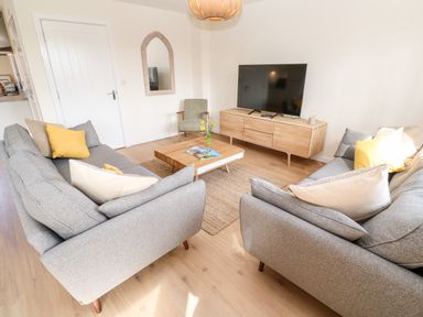 A living room with two gray sofas yellow and white pillows a wooden coffee table and a television on a wooden TV stand at The Bright House in St Eval near St Columb Major