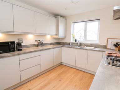 A kitchen with white cabinets a countertop with microwave coffee machine kettle sink and gas stove at The Bright House in St Eval near St Columb Major