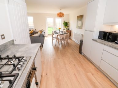 A kitchen and dining area with a gas stove, microwave, dining table with chairs, sofa, and glass doors leading to a garden at The Bright House in St Eval near St Columb Major