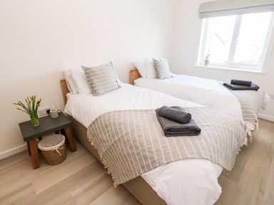 A bedroom with two single beds side by side each with striped cushions and folded towels at The Bright House in St Eval near St Columb Major