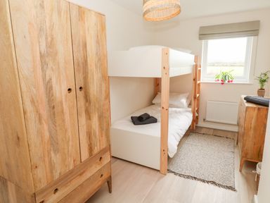 A bedroom with a wooden wardrobe bunk bed dresser and window at The Bright House in St Eval near St Columb Major