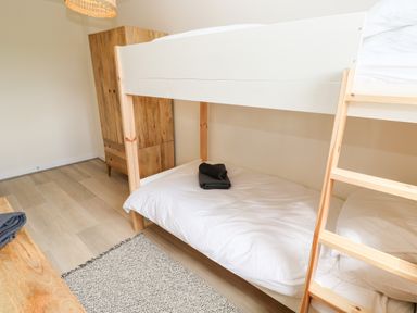 A bedroom with a white bunk bed a wooden wardrobe and a rug on the floor at The Bright House in St Eval near St Columb Major