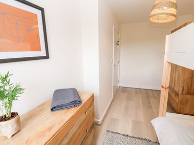 A bedroom with wooden dresser, potted plant, folded blanket, bunk bed, door and hanging light at The Bright House in St Eval near St Columb Major