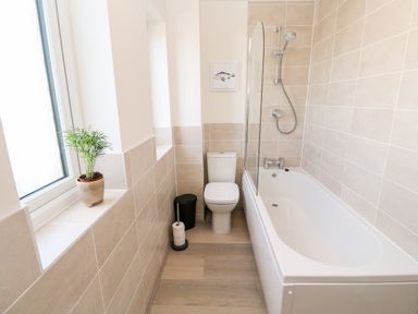 A bathroom with a bathtub shower combination toilet plant on the window sill at The Bright House in St Eval near St Columb Major
