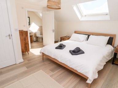 A bedroom with a double bed and two folded towels on the bed a skylight window a wooden cabinet an open door showing a bathroom at The Bright House in St Eval near St Columb Major