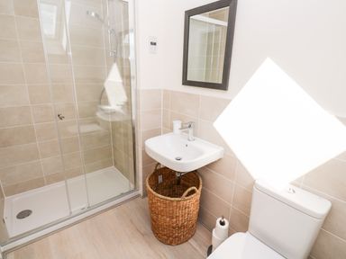 A bathroom with a glass enclosed shower a sink with a wicker basket underneath a toilet and a mirror at The Bright House in St Eval near St Columb Major