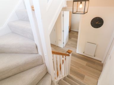 A stairway with carpet leading down to a hallway with wooden floor a clock on the wall and a radiator at The Bright House in St Eval near St Columb Major