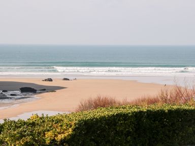 A sandy beach with rocks and people near the ocean with greenery in the foreground at The Bright House in St Eval near St Columb Major