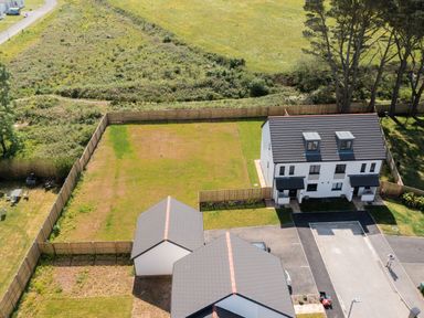A fenced backyard with two houses and a driveway in a rural area at The Bright House in St Eval near St Columb Major