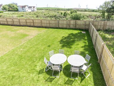 A garden with two round tables and eight chairs on the grass enclosed by a wooden fence at The Bright House in St Eval near St Columb Major