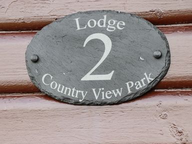 A black oval sign with white text reading Lodge 2 Country View Park on a wooden surface at Lodge Two Country View Park in Graveney
