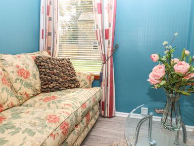 A floral patterned sofa with a textured cushion beside a window with curtains and a glass table with a vase of flowers in a room with blue walls at Lodge Two Country View Park Graveney