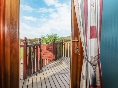 A wooden deck with a gate outside a glass door with patterned curtains at Lodge Two Country View Park in Graveney