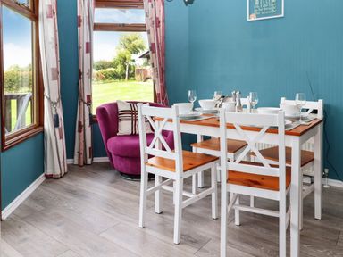 A dining area with a wooden table set for four and a purple armchair by windows at Lodge Two Country View Park Graveney