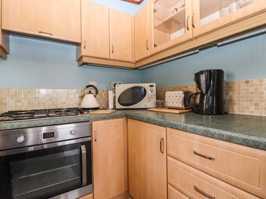 A kitchen corner with a stove oven kettle microwave toaster coffee maker and wooden cabinets at Lodge Two Country View Park in Graveney
