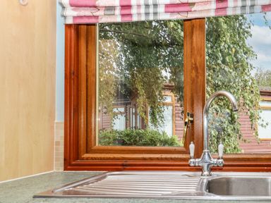 A kitchen sink with a chrome faucet under a wooden framed window with a view of greenery and a wooden exterior at Lodge Two Country View Park in Graveney