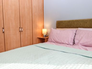 A bedroom with a bed with pink pillows and light green quilt and a wooden wardrobe and a bedside table with a lamp at Lodge Two Country View Park in Graveney