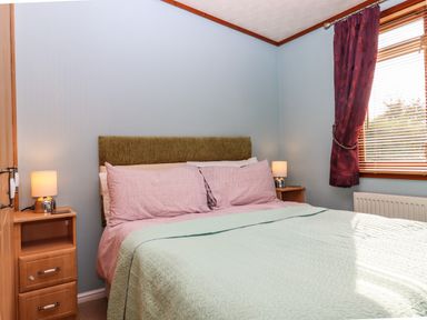 A bedroom with a bed with patterned pillows and a light green quilt and bedside tables with lamps at Lodge Two Country View Park in Graveney