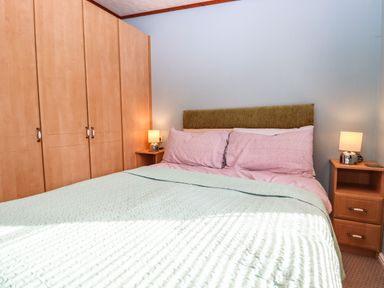 A bedroom with a double bed with pink pillows green bedcover two bedside tables with lamps and a wooden wardrobe at Lodge Two Country View Park in Graveney