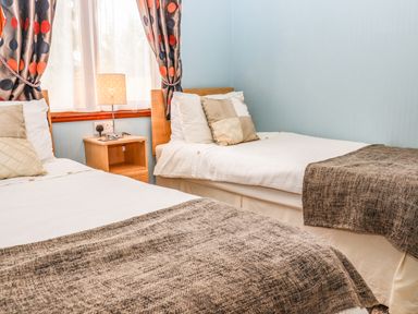 A bedroom with two single beds a nightstand with a lamp and a window with polka dot curtains at Lodge Two Country View Park in Graveney