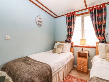 A bedroom with two single beds a bedside table with a lamp and a window with patterned curtains at Lodge Two Country View Park in Graveney