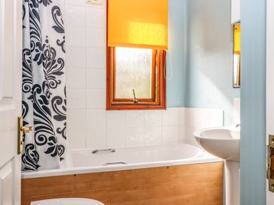 A bathroom with a bathtub with wooden paneling a patterned shower curtain a window with a yellow blind and a white sink at Lodge Two Country View Park in Graveney